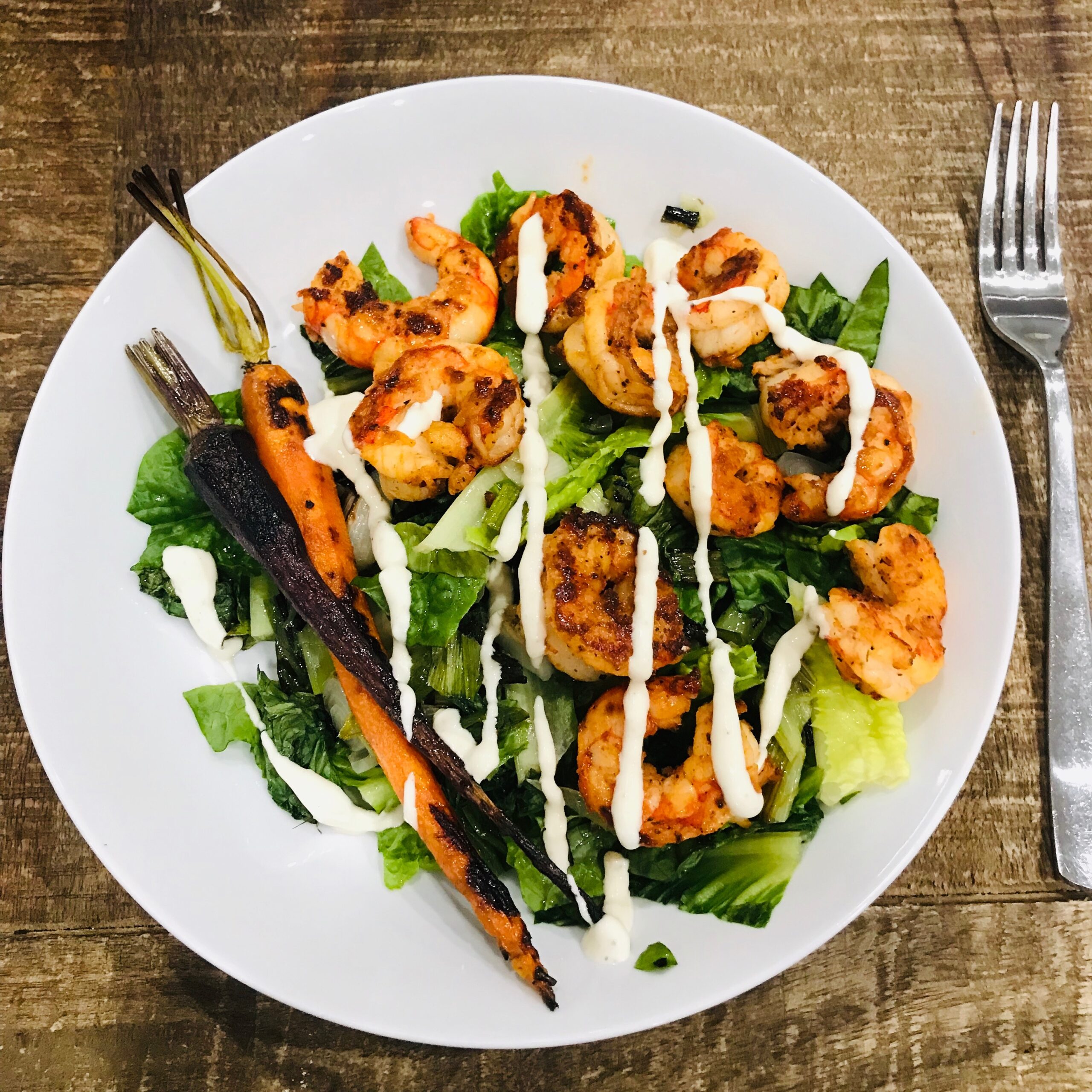 Grilled Shrimp with charred carrots on romaine lettuce with ceasar dressing on a plate